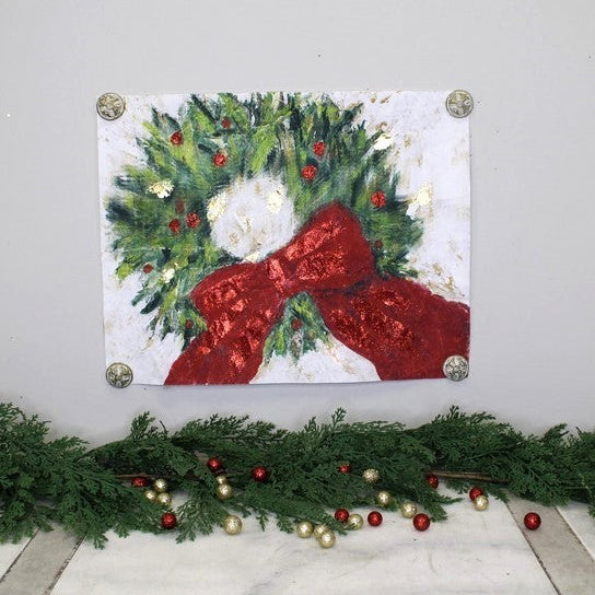 A square canvas art print featuring a festive green wreath with a large red bow, mounted on a light gray wall above a holiday garland with red and gold ornaments.