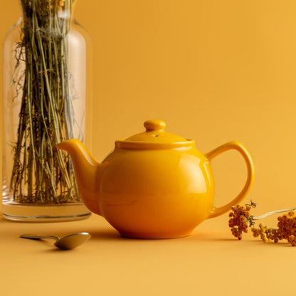 mustard teapot on a yellow background arranged with dried flowers, a spoon, and a vase.