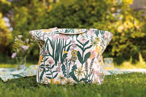 bees and blooms tote set on a grassy lawn next to a picnic blanket.