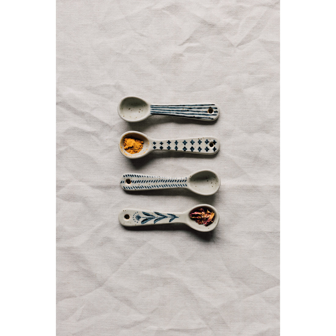 Four ceramic mini spoons with different blue patterns, displayed on a linen surface.