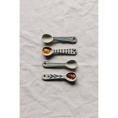 Four ceramic mini spoons with different blue patterns, displayed on a linen surface.