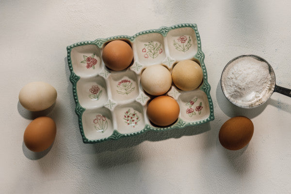 top view of the camilla egg holder partially filled with eggs and a measuring cup filled with flour and a few eggs set next to it.