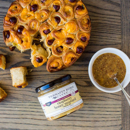 jar of Raspberry Honey Mustard on a table with pastries.