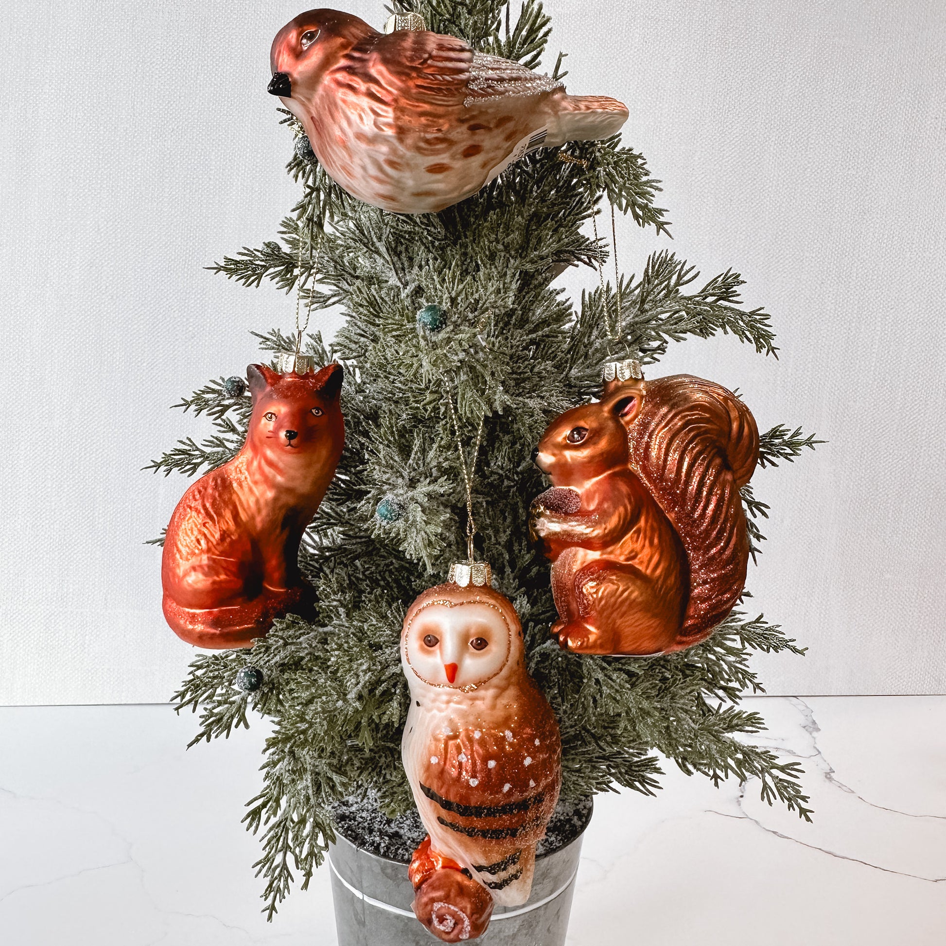 set of woodland animal ornaments including a fox, owl, squirrel, and bird in a tree.