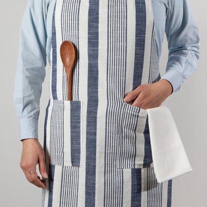 person wearing blue and white striped apron with their hand in one pocket and a wooden spoon in the other.