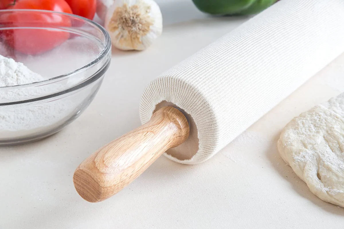 Rolling pin with cover on a white surface with flour and vegetables in the background