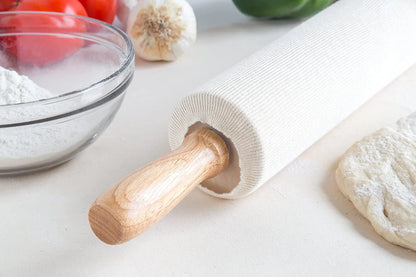 Rolling pin with cover on a white surface with flour and vegetables in the background