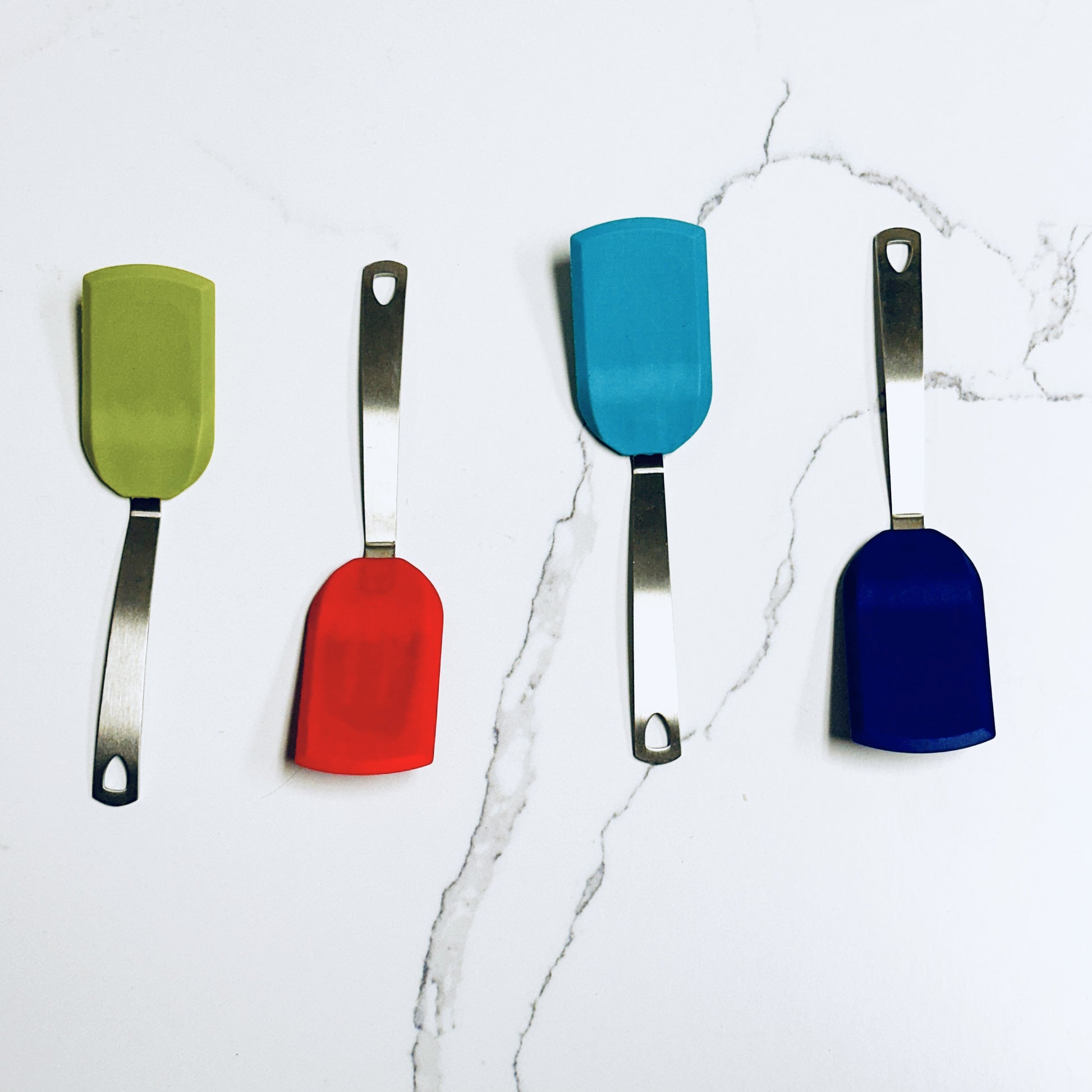 four mini silicone turners in green, red, turquoise, and blue on a marble background.