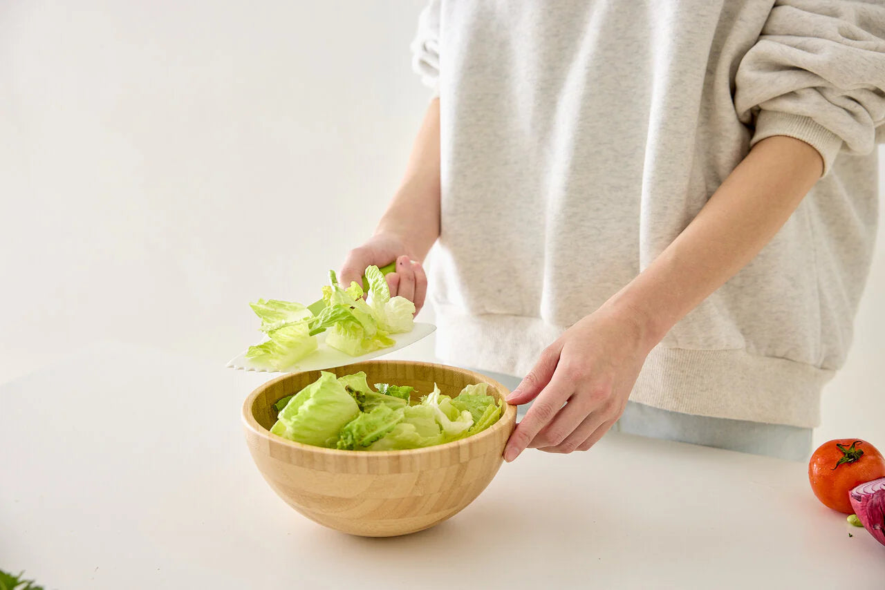 Person preparing lettuce in a wooden bowl on a white surface