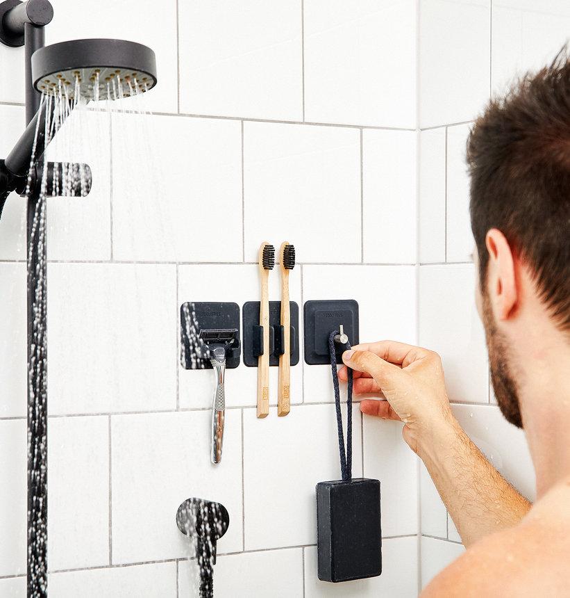 black silicone razor holder, toothbrush holder, and hook in a white tiled shower.