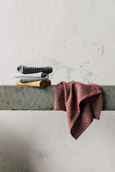 Stack of folded towels set on a wooden ledge with another towel draped over it.
