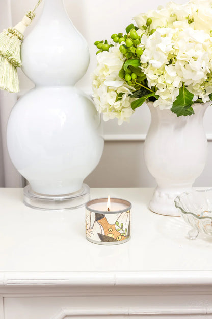 lit Birch & Bloom Tin Candle set on a side table with white vases