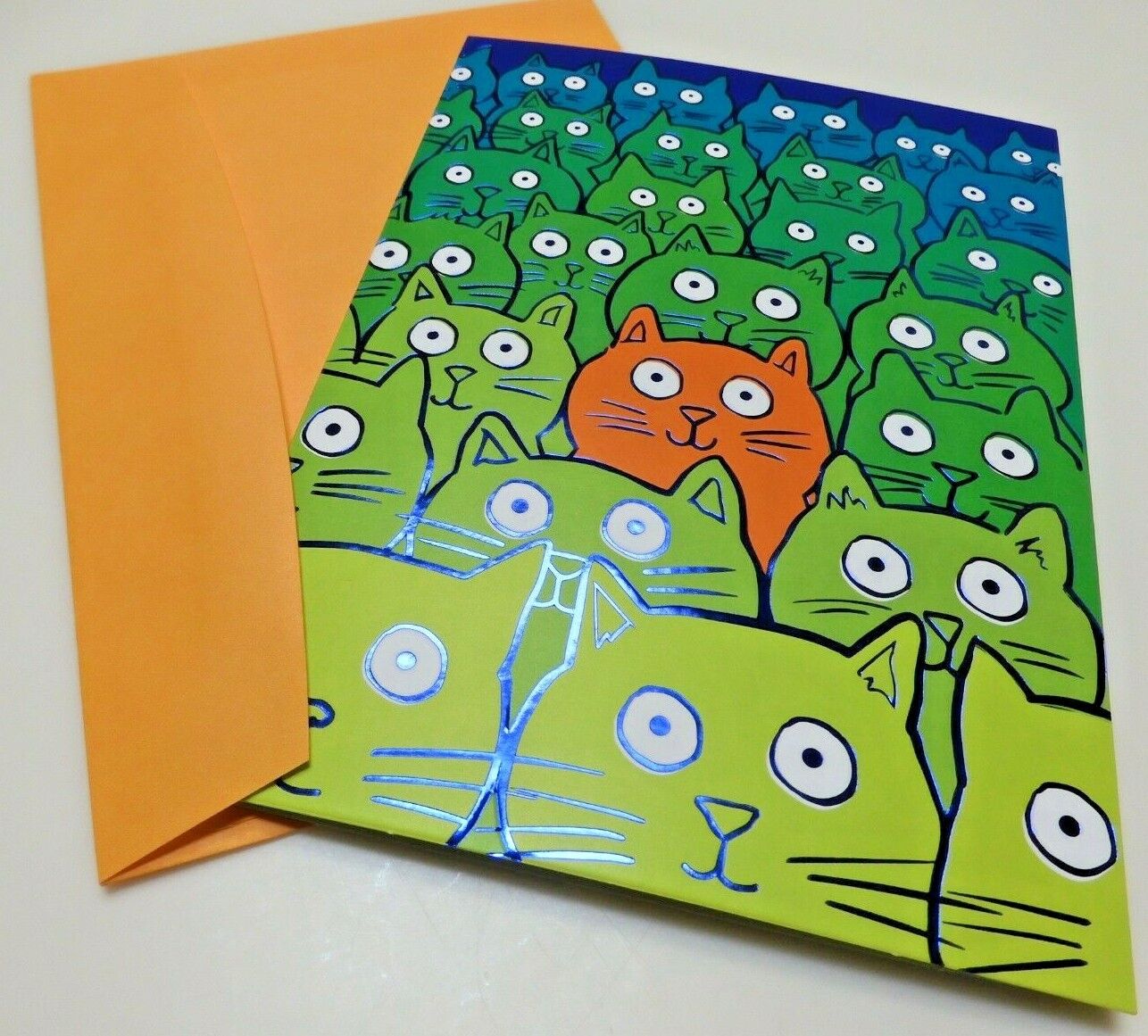front of card is drawing of six rows of green cats and one orange in the middle