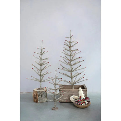 3 sizes of silver tinsel trees arranged with a bowl of ornaments and wooden elemants.