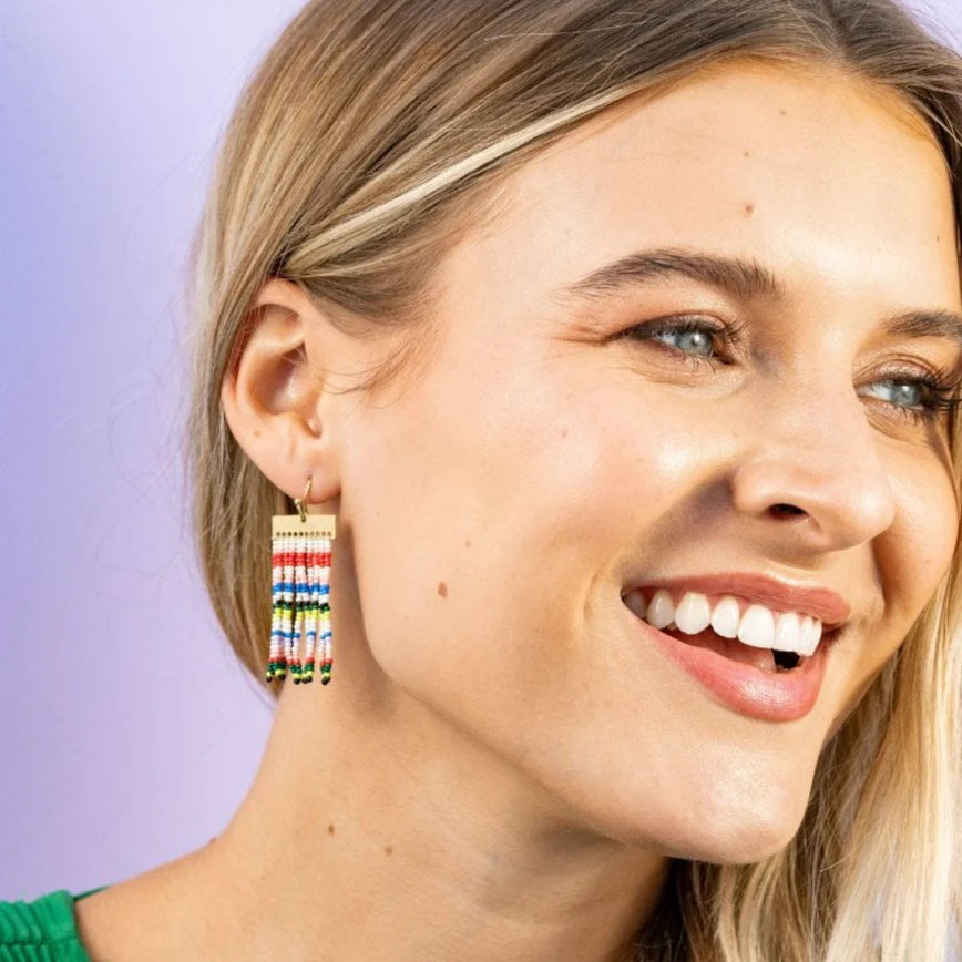 smiling person wearing colorful beaded earrings with a purple background