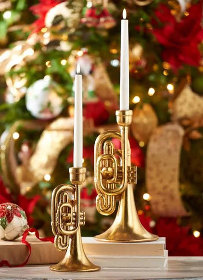 both sizes of trumpet candle holders with white tapers in them and a christmas tree in the background.