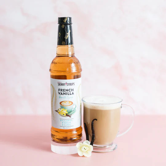 bottle of french vanilla skinny syrup set next to a glass mug of a coffee beverage and a vanilla bean.