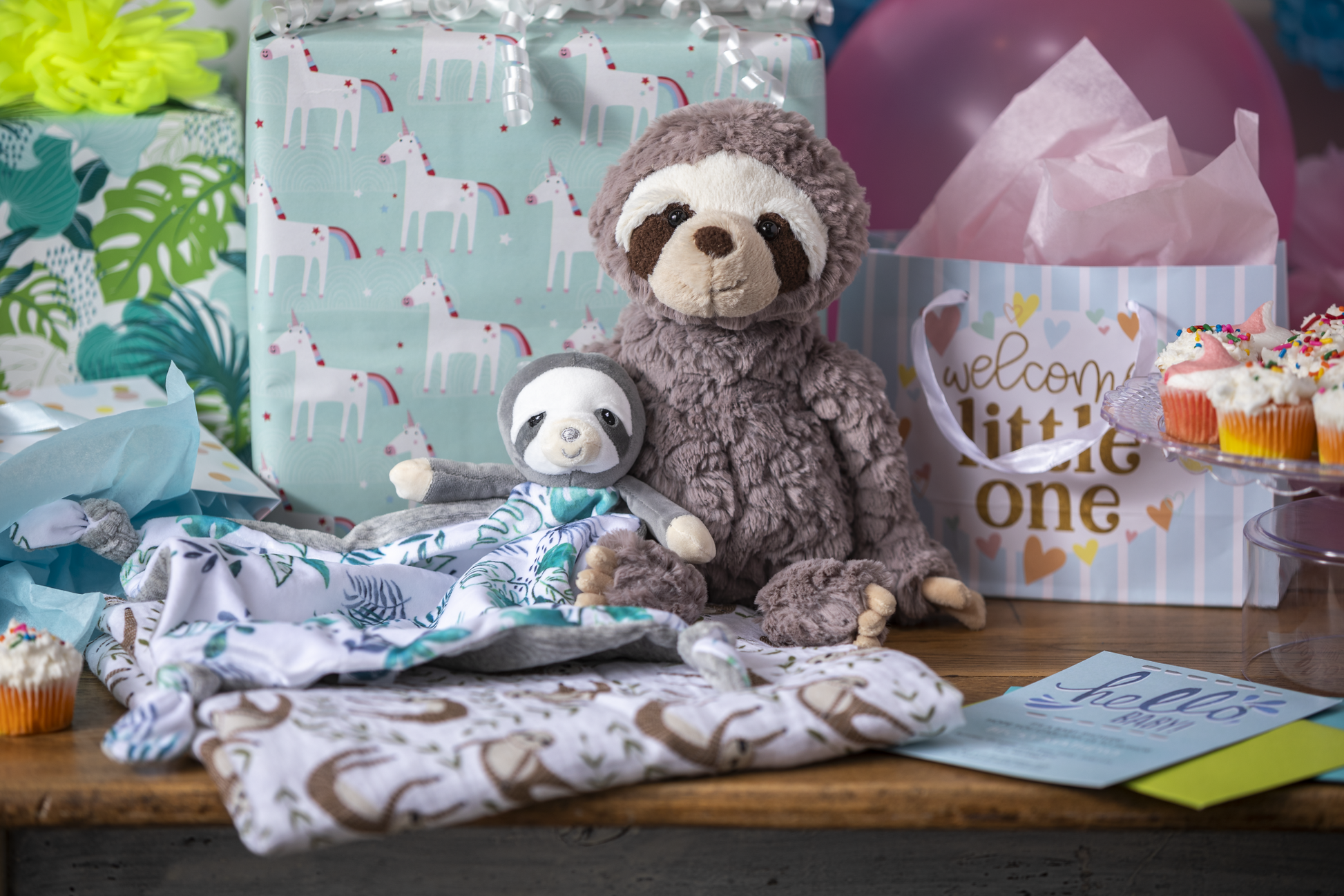 Little Knottie Sloth Blanket displayed next to a slot plush toy and wrapped gifts