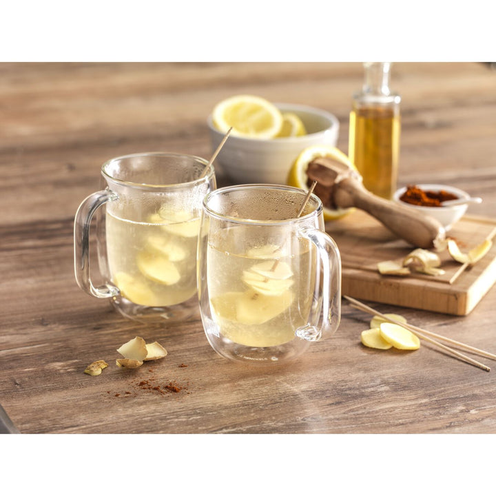 2 sorrento mugs filled with beverage and garnish on a wooden table with lemons and a juicer in the background.