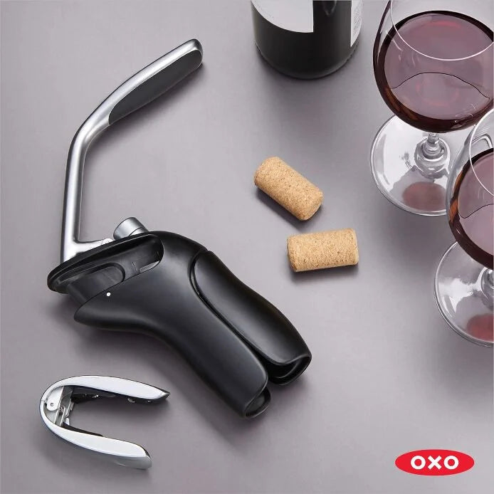 Vertical Lever Corkscrew and foil cutter set on a table with corks and glasses of wine