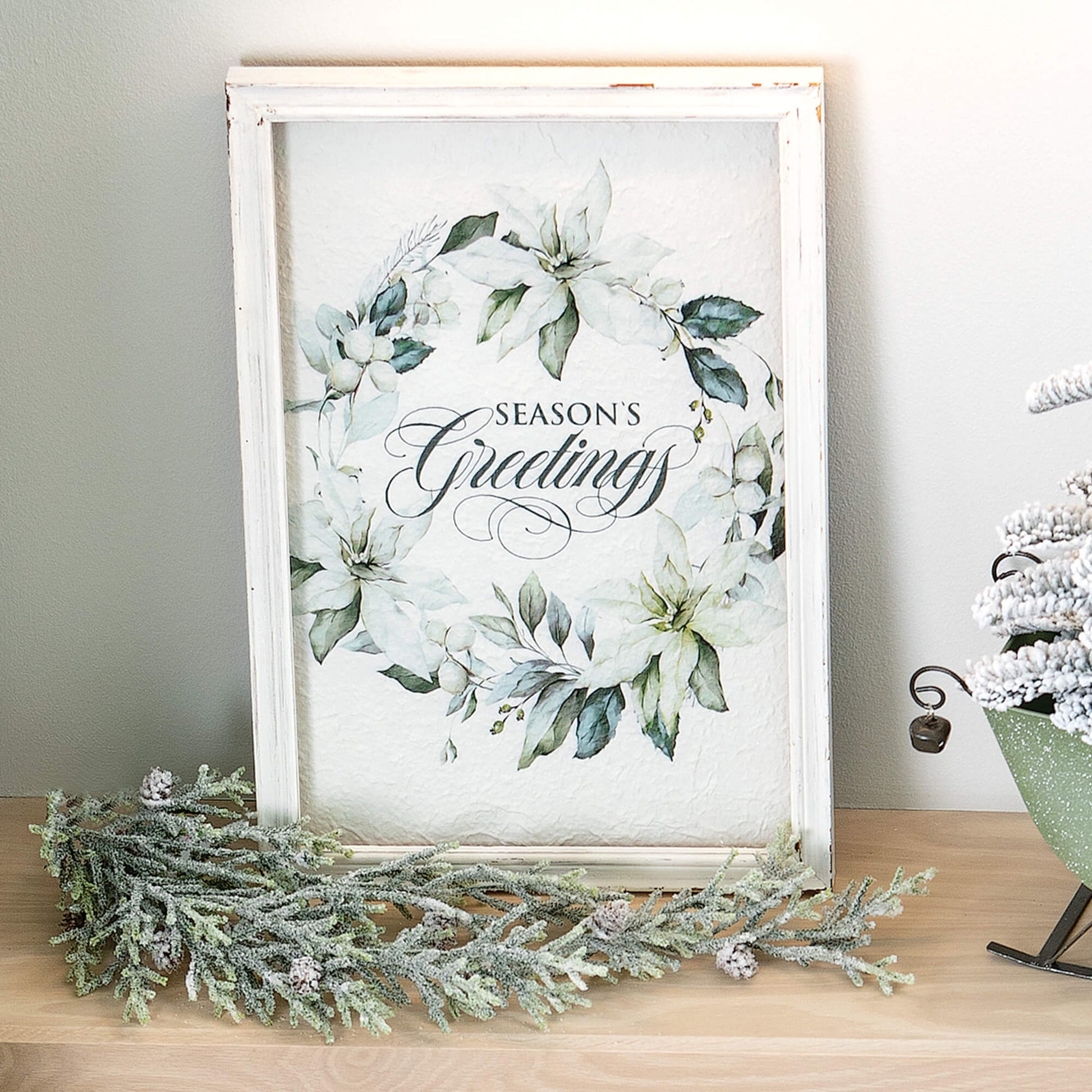 full snowy pine swag displayed with a white framed picture, green sleigh on a light wood shelf