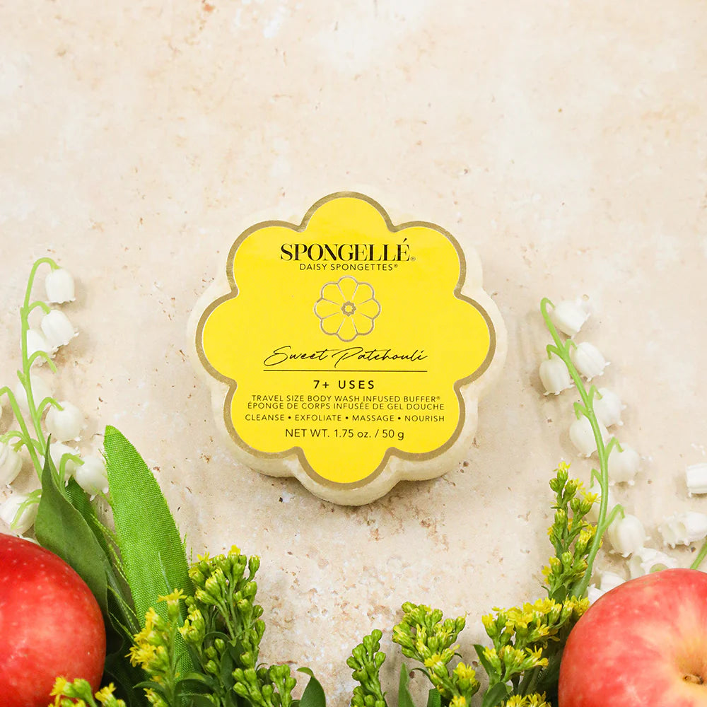 Spongellé body sponge with yellow label on a textured beige background with apples and greenery.