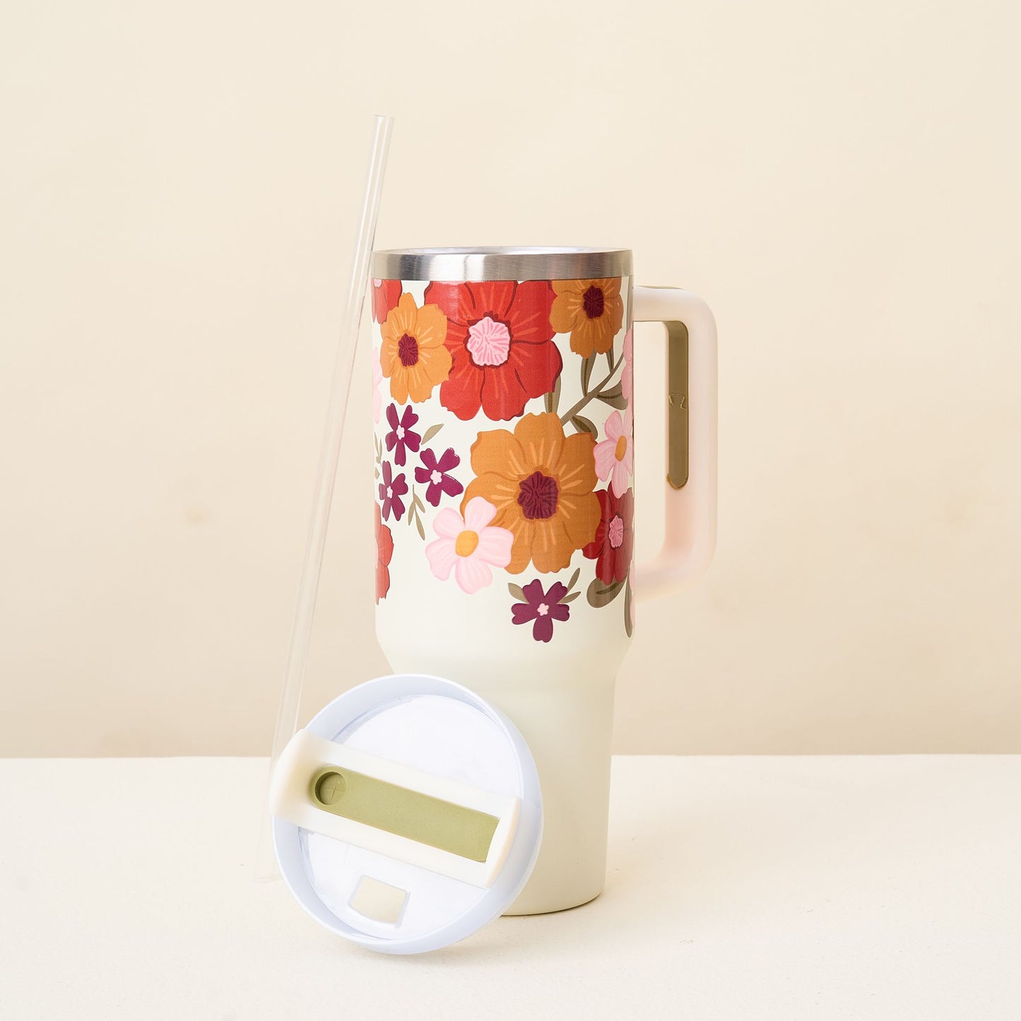 cream tumbler with floral pattern around the top with its lid resting against it on a light background.