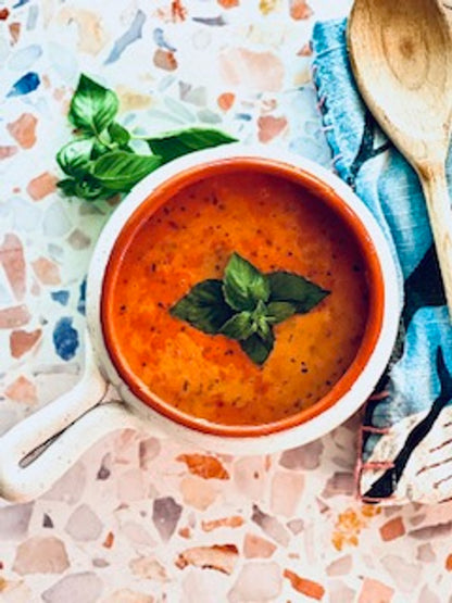 bowl of tomato basil soup set on a counter with a cloth napkin and sprig of basil