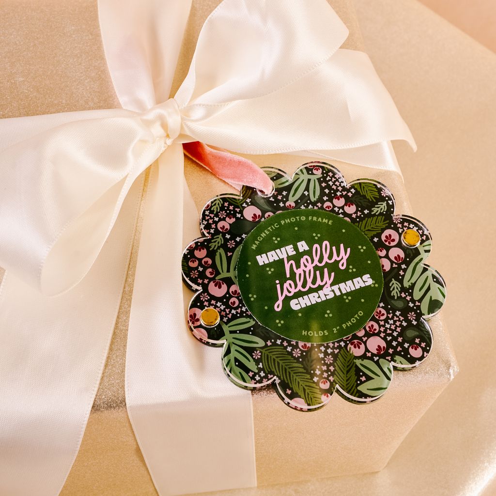 flat scallop edge ornament with pink and green holly imagery tied on a package