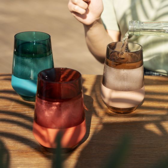 3 colors of wine freeze glasses set on a table, a person is pouring wine into one of them.