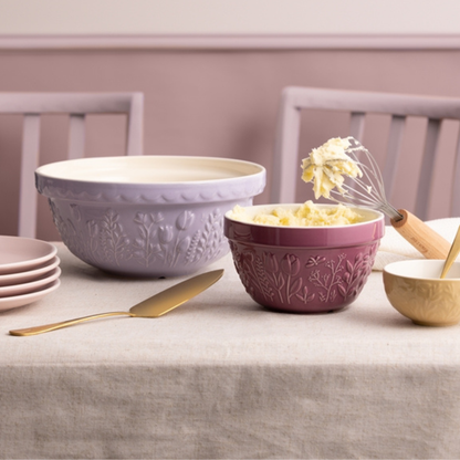In the Meadow Purple Floral All Purpose Bowl filled with butter set on a table with a larger and small bowl and a stack of plated around it.