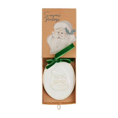 oval ornament with a raised santa design laying in its box.