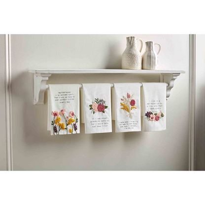 4 styles of funny mom towels hanging under a white shelf that has vase set on it.
