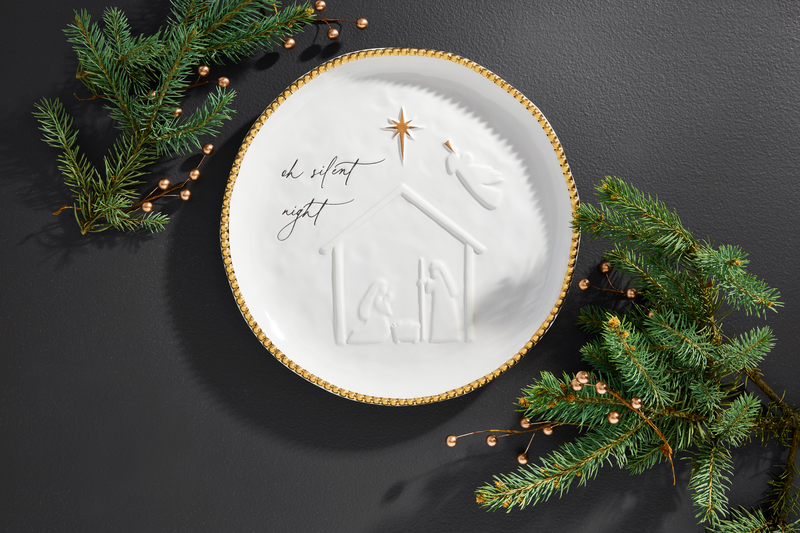 Silent night nativity platter set on a dark gray background with sprigs of greenery around it.