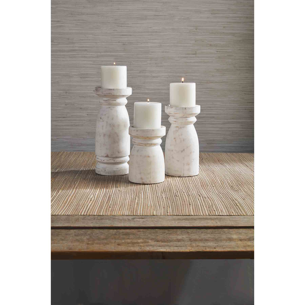 3 sizes of wooden candlesticks with washed white finish arranged on a table with lit candles on them.