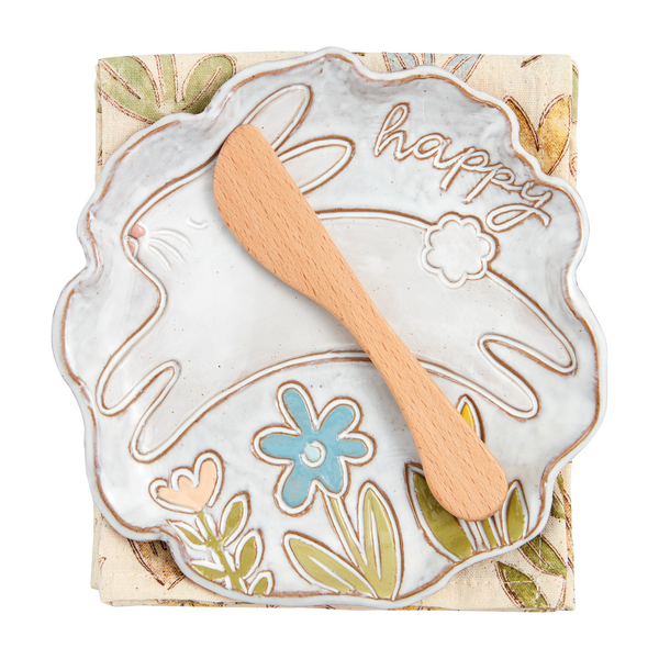 white plate with a jumping bunny, flowers, and "happy" on it set on a folded towel with a wooden spreader.