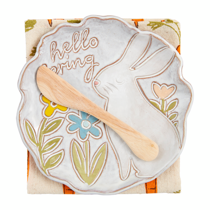 white plate with textural image of a sitting bunny, flowers, and "hello spring" on it set on a folded towel with a wooden spreader.