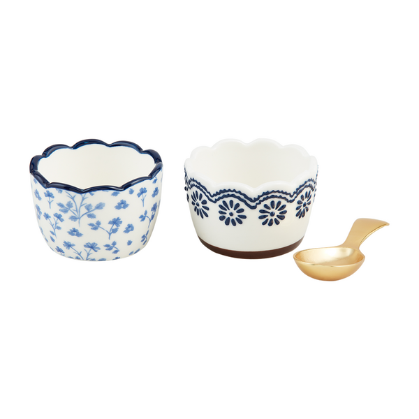 2 white ramekins, one with a light blue floral pattern all over, the other with a dark blue geometric patter around the rim, with a gold spoon set next to the.