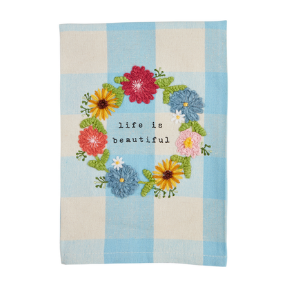 blue check hand towel with an embroidered wreath of flowers and "life is beautiful" in the center.