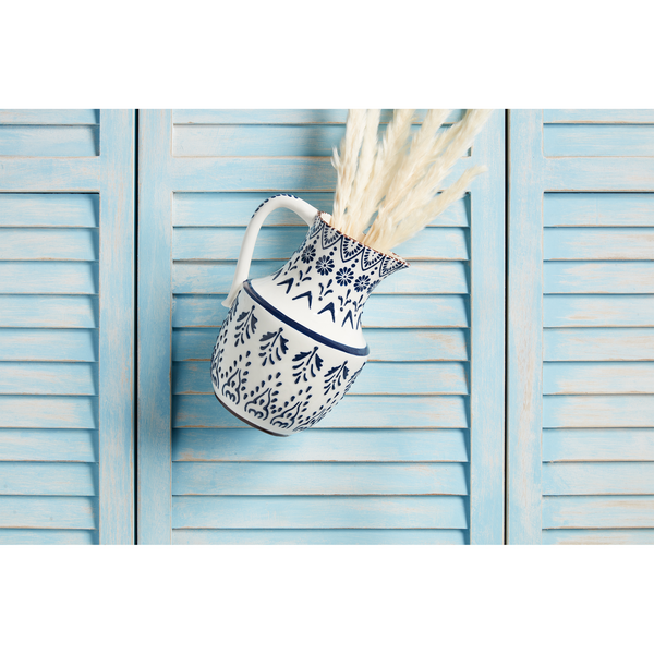 blue and white pitcher with dried plumes in it laying on a blue slat background.