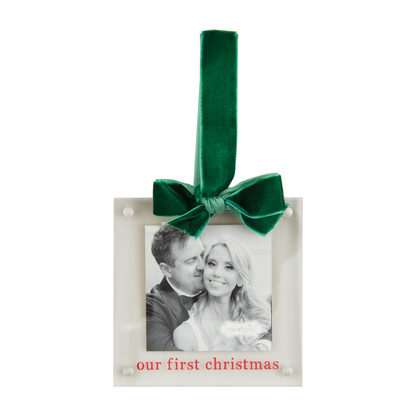 "our first christmas" acrylic frame ornament hanging from a green velvet ribbon.