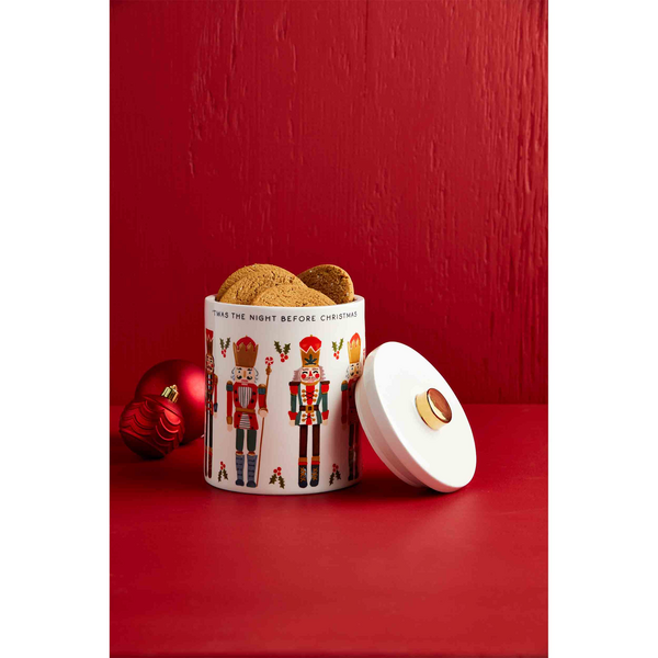 nutcracker cookie jar set on a red table filled with cookies and its lid leaning against it.