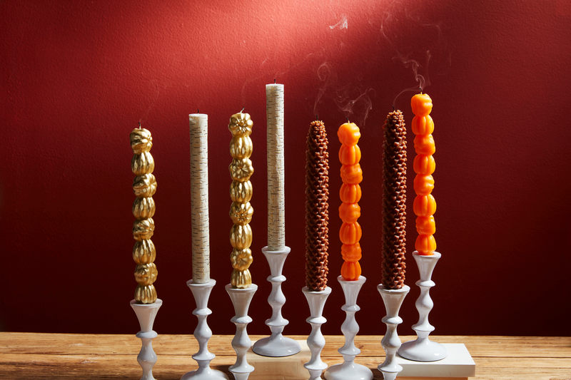 4 styles of taper candles in white taper holders arranged on a wooden table.