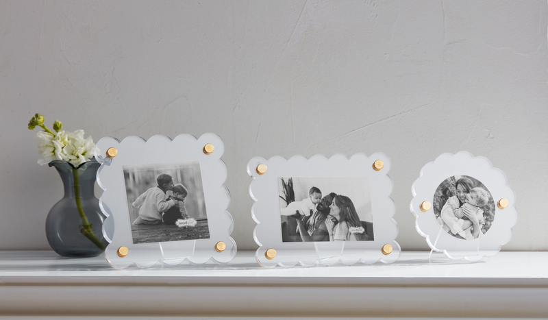 Three acrylic picture frames with scalloped edges and brass corner rivets displayed on a white surface, holding various photos.