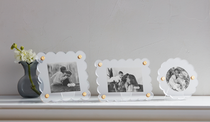 Three acrylic picture frames with scalloped edges and brass corner rivets displayed on a white surface, holding various photos.