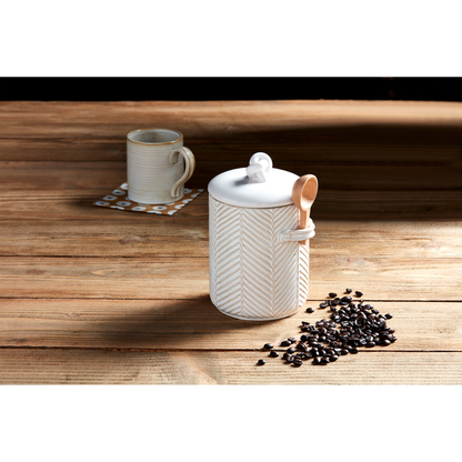 coffee canister set on a wooden surface with coffee beans scattered around it and a coffee mug in the background.