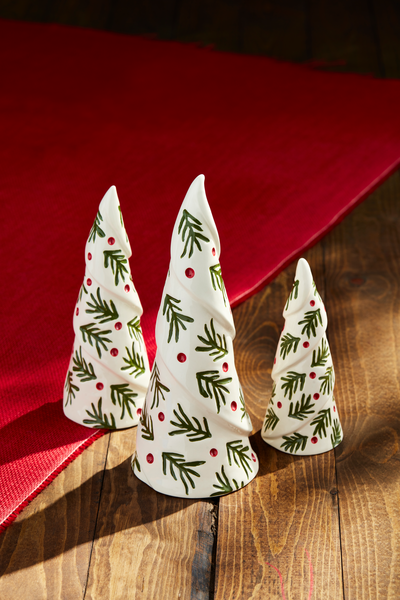 3 sizes of ceramic holly tree sitters arranged on a wooden table with a red runner.