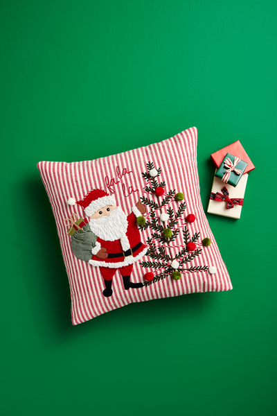 fa la la Santa pillow shown on a green background with small gifts next to it.