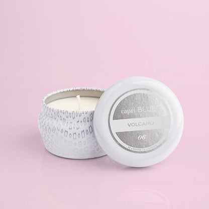 Volcano Signature White Mini Tin Candle with lid resting against it on a light pink background.