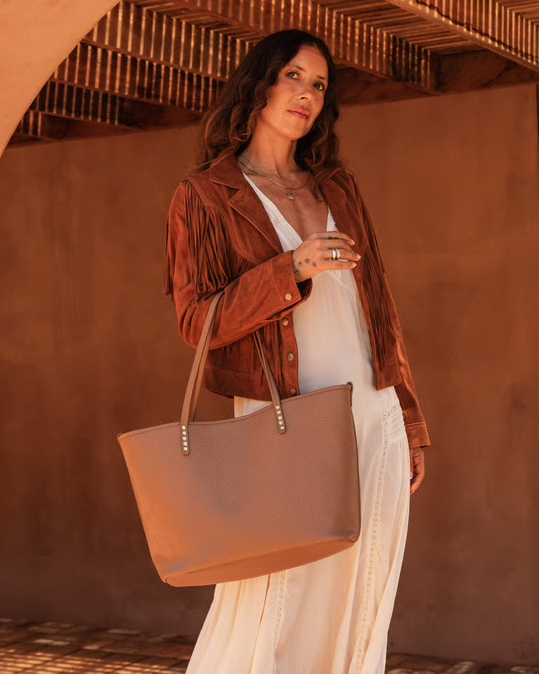 Woman holding a beige tote bag against a warm-toned wall.